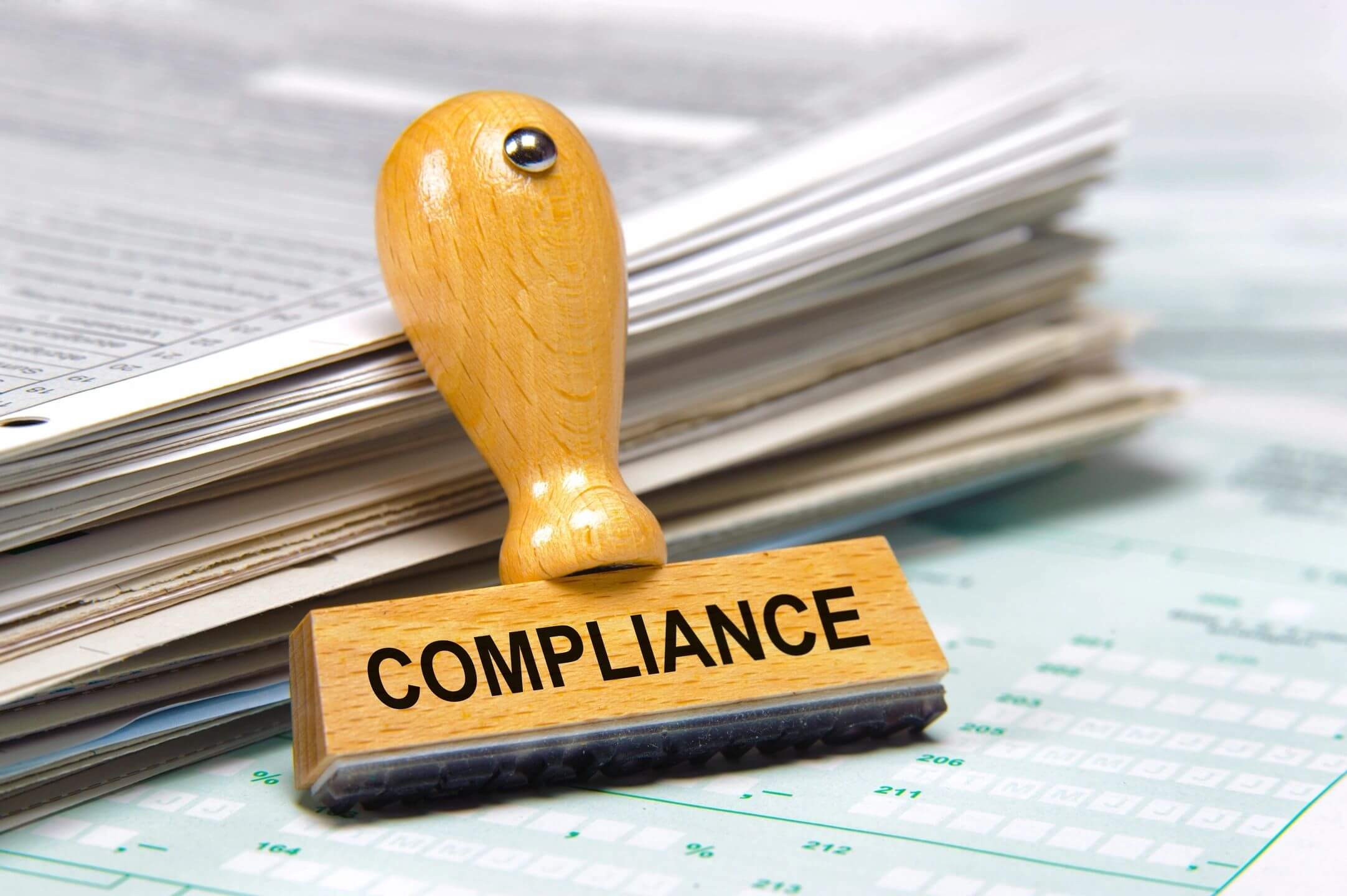 A wooden stamp with 'COMPLIANCE' on documents.