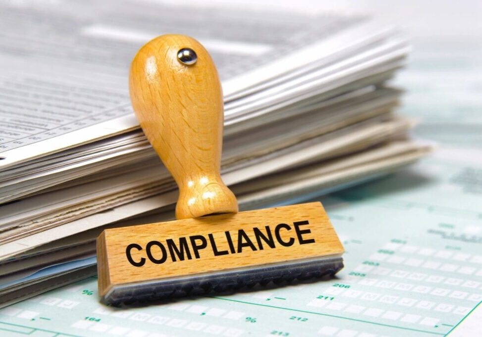 A wooden stamp with 'COMPLIANCE' on documents.